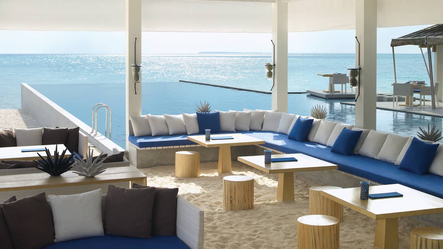 Long L-shaped booth with blue and white cushions, tables on sand in Seabar lounge