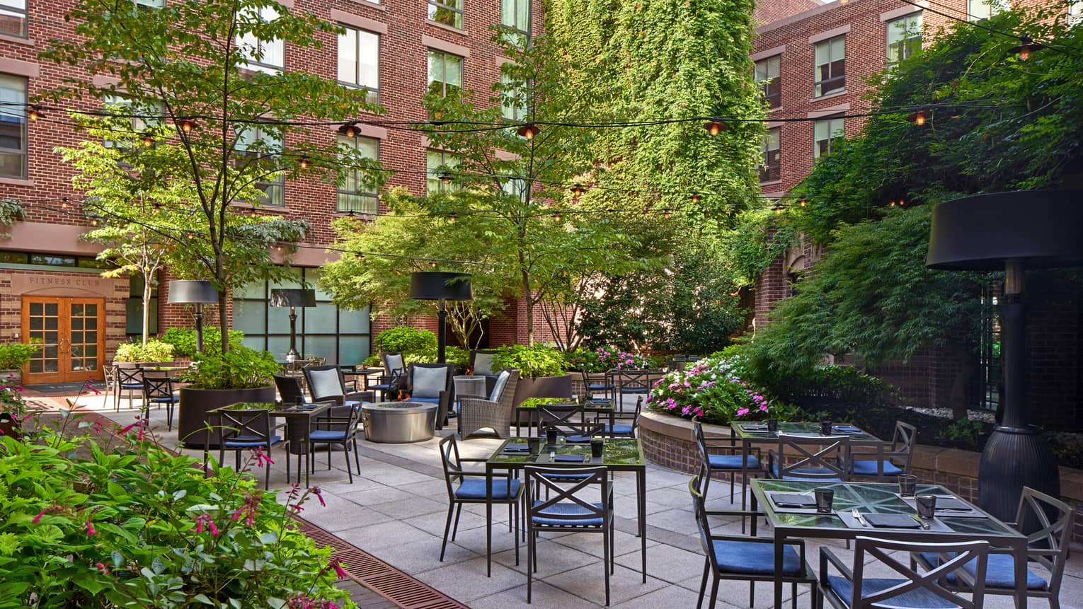 An outdoor eating area with metal chairs and glass tables surrounded by plants.