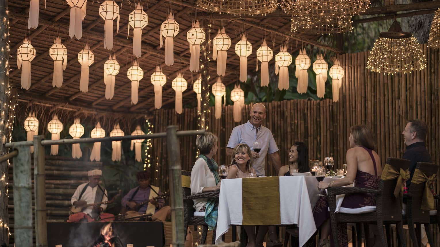 A group of people sitting at a table enjoying a meal in outdoor pavilion decorated with lanterns