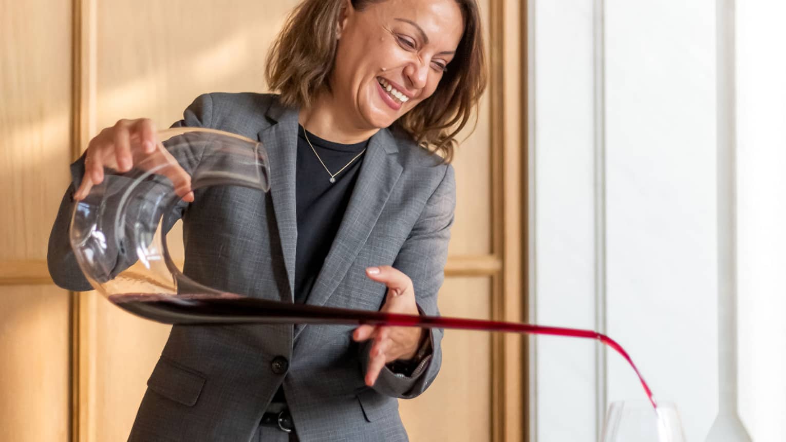 Brasserie Palmier Bar sommelier smiles, pours red wine from long decanter into wine glass on table