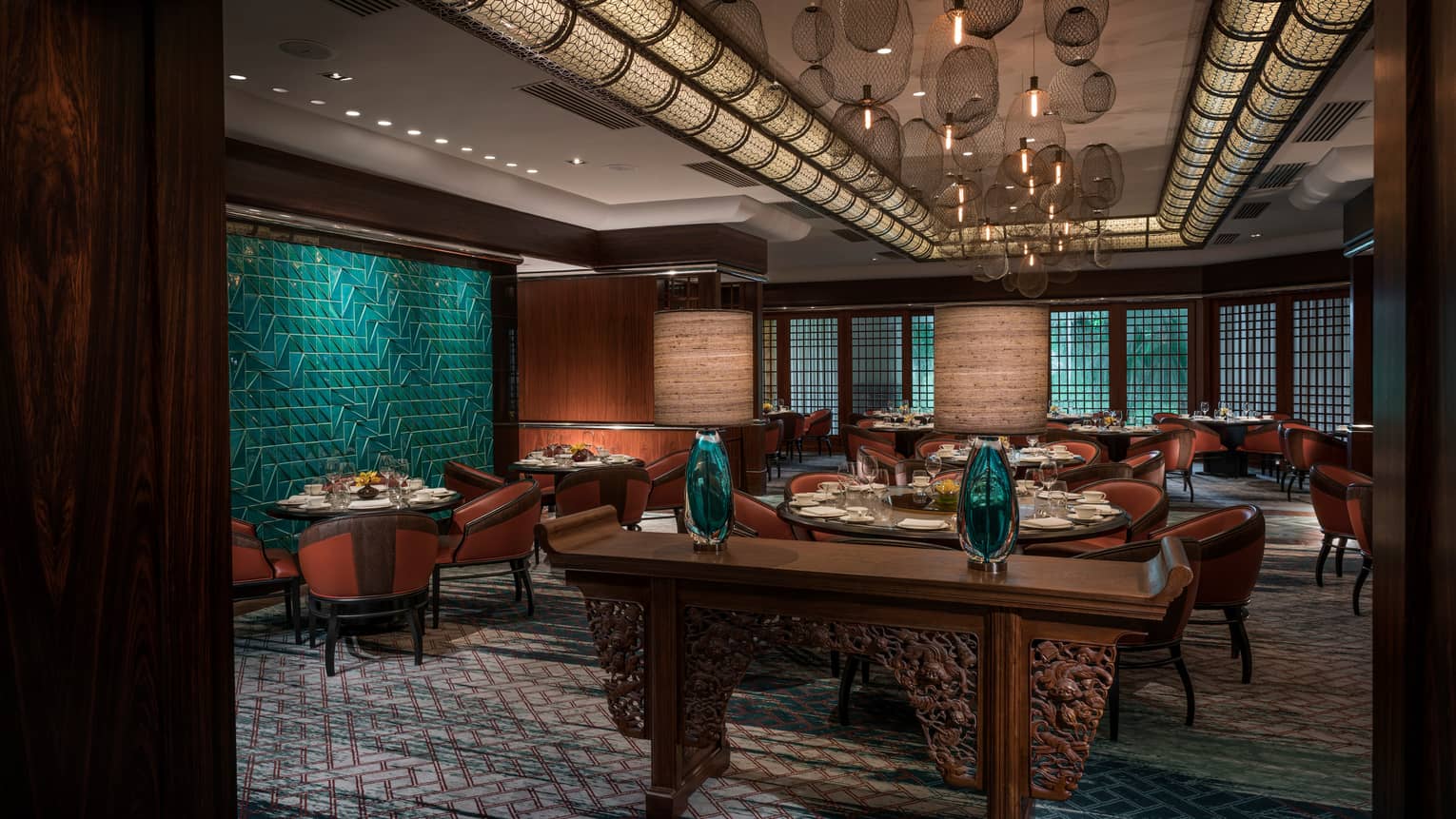 Carved wood console with glass vases in front of dining room, green tile wall