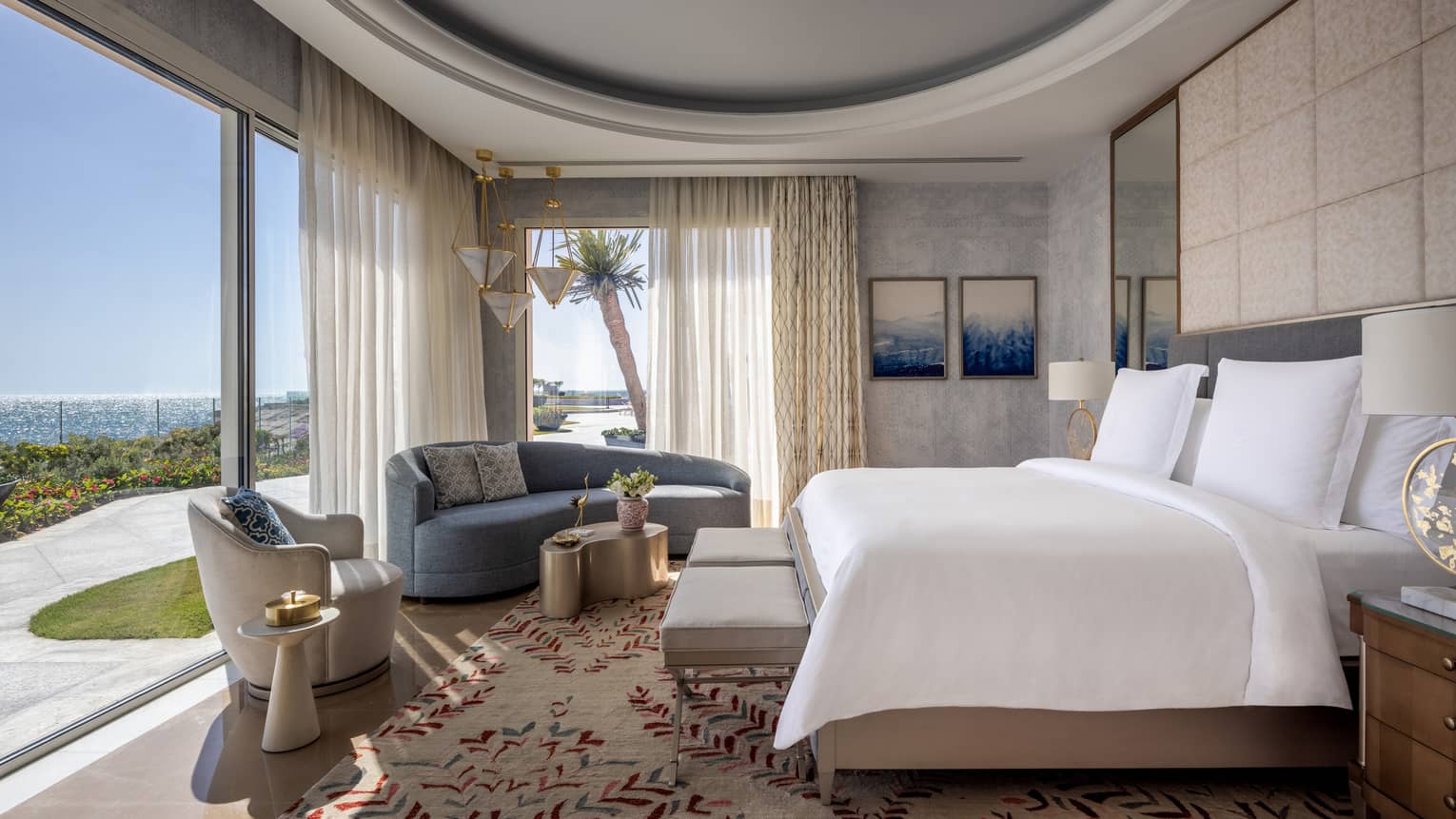 The Palace open air bedroom with king bed and white linens, blue sofa, cream armchair, sliding glass door to patio with natural light