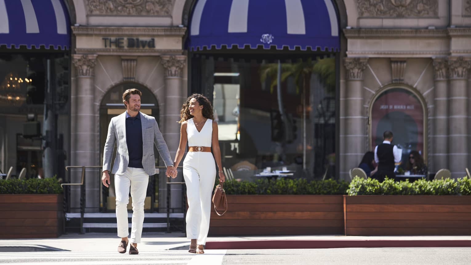 A man and woman holding hands while walking across a street.