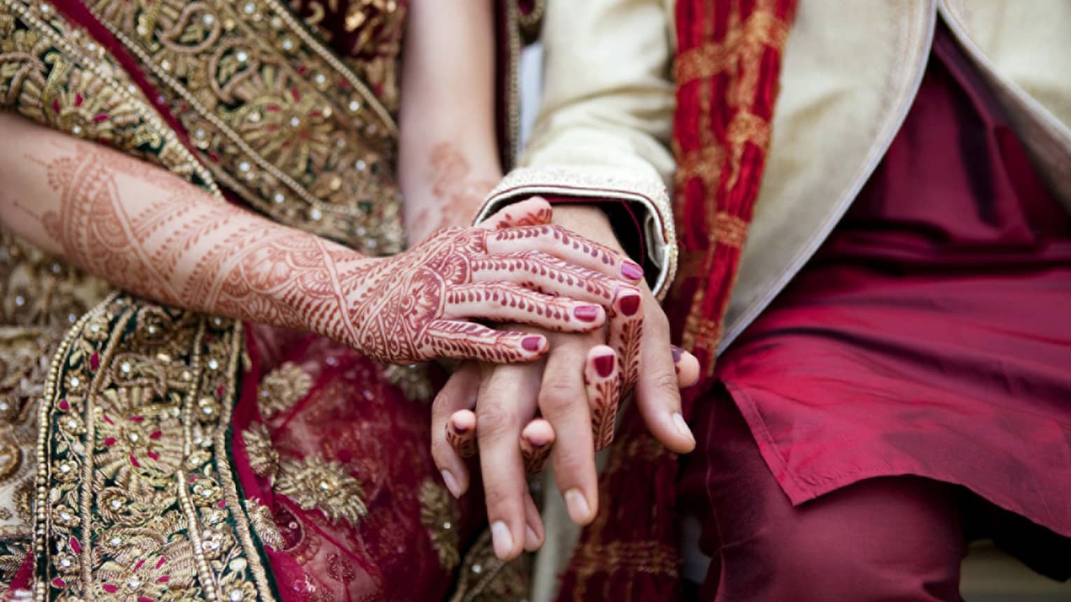 Indian wedding ceremony, bride with henna designs on arm holds groom's hands