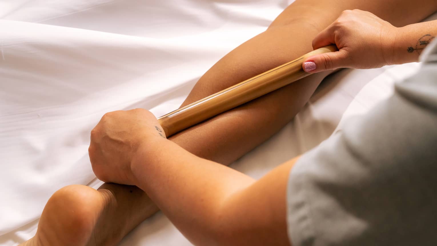 Pair of hands rolling a bamboo stick over a person's calf muscle