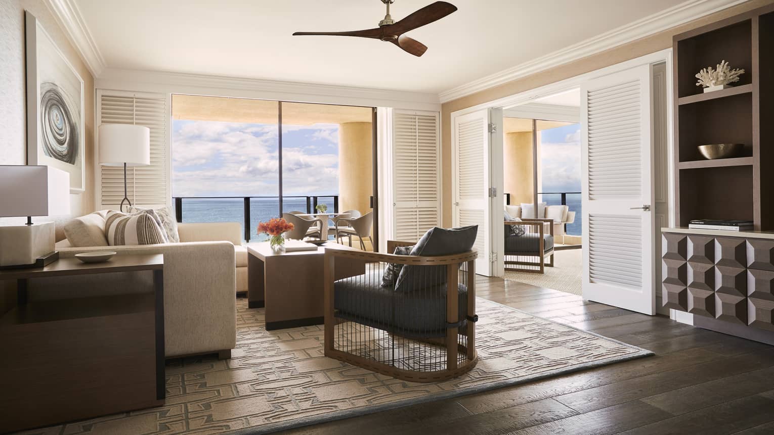 Elegant living area with neutral furnishings, ceiling fan, ocean view and adjoining room through open double doors