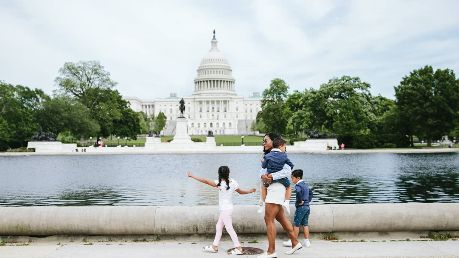 Woman and three children walk in front of the Capitol reflecting pool in Washington, DC, with Capitol building in background