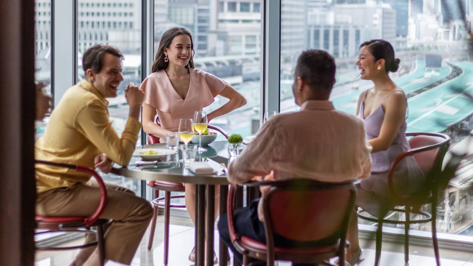 Two couples laugh and drink wine at Maison Marunouchi with views of the Shinkansen trains behind them