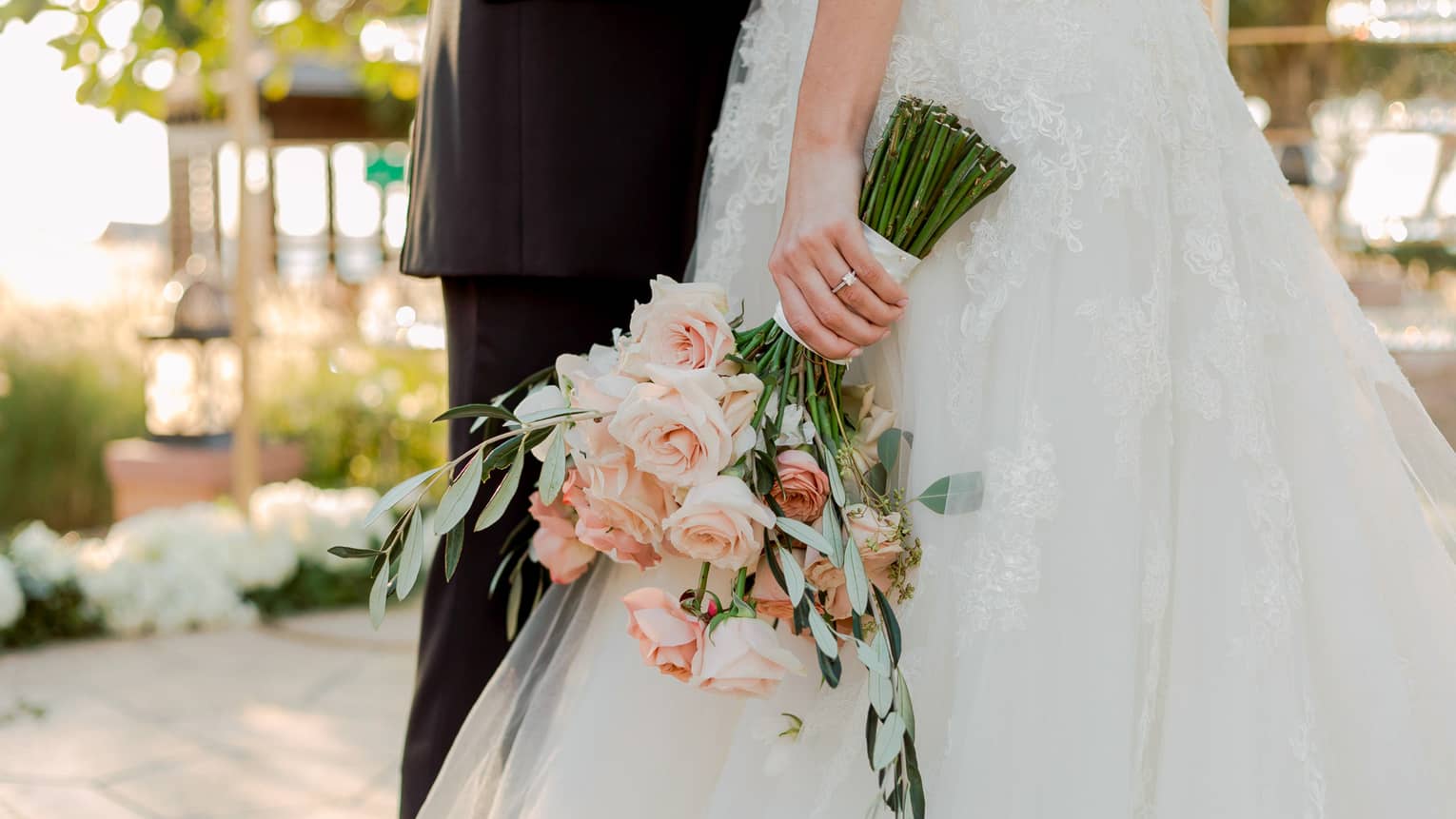 Groom and bride holding wedding floral bouquet of long-stemmed pink roses