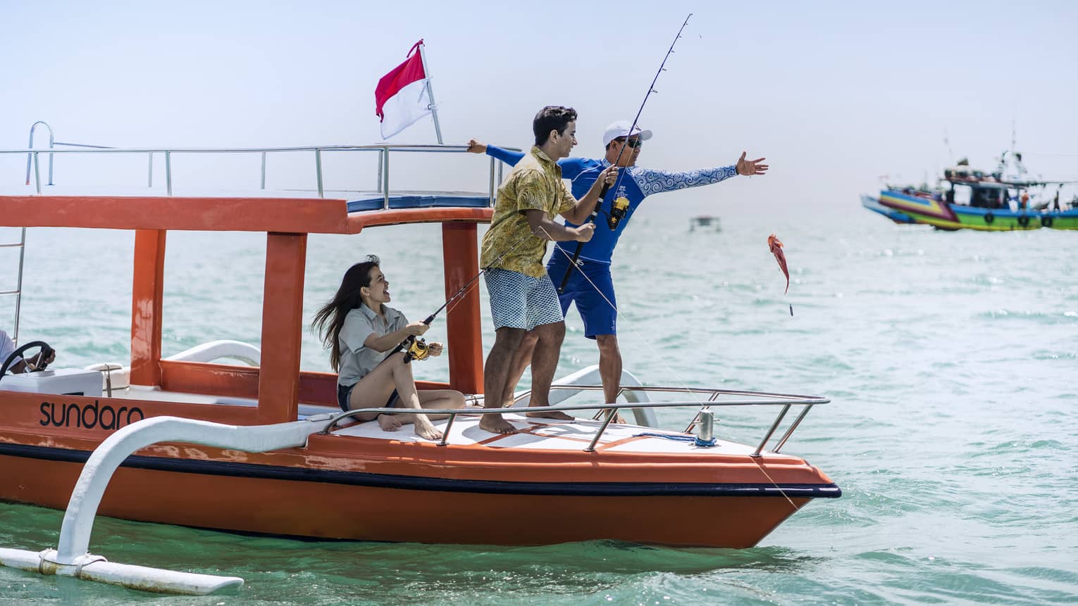 Tour guide teaches two guests to fish on a traditional jukung fishing boat on the open ocean