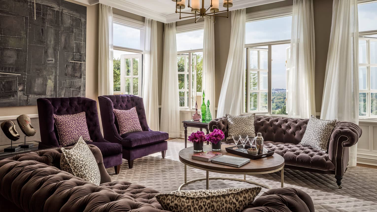 Presidential Suite tufted velvet sofas and armchairs around coffee table. sunny corner windows, curtains