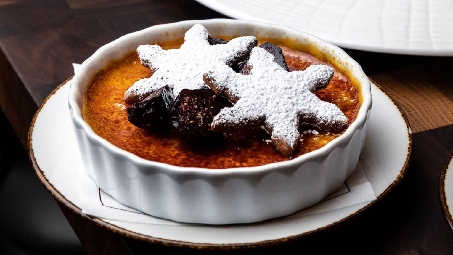 Vanilla Cr�me Br�l�e in a round white dish topped with figs and powdered-sugar-covered snowflake cookies