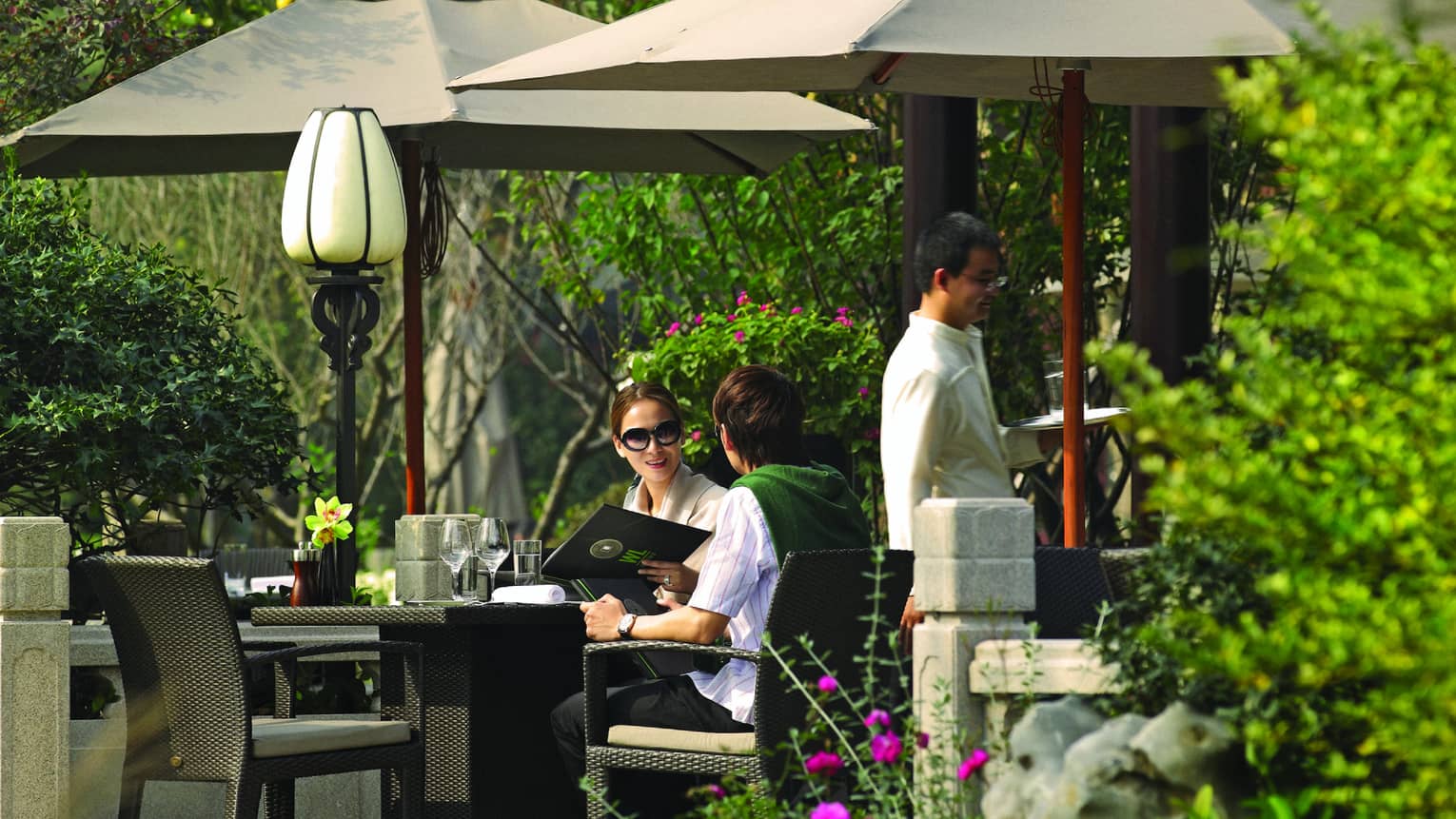 Couple holds menu at patio dining table under umbrellas, pavilion