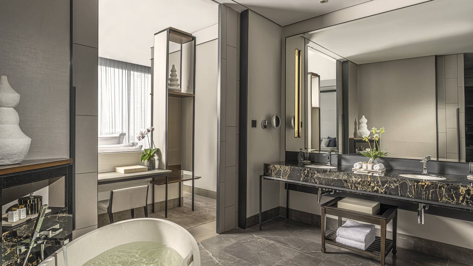 Bathroom, large mirror over black marble double vanity, standalone white tub, opening to bedroom