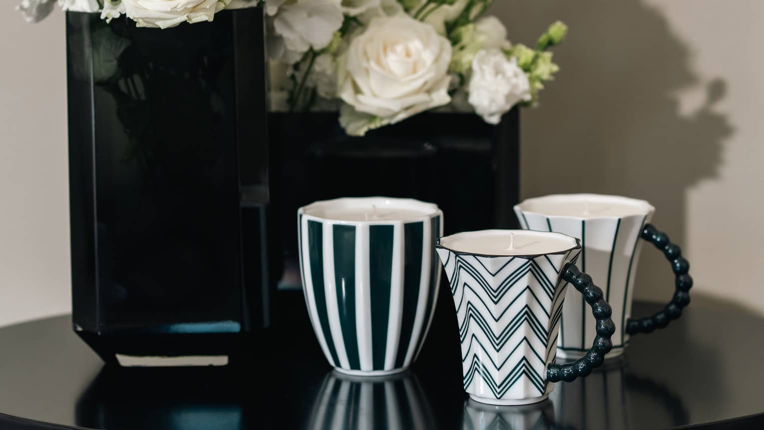 Patterned mug candles on black table beside white roses in black vases