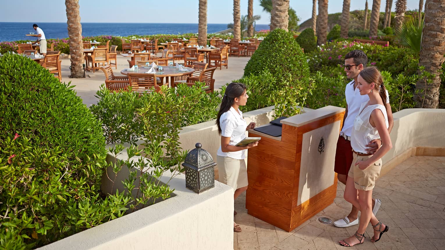 Host greets couple with arms around each other at Reef Grill outdoor reception stand