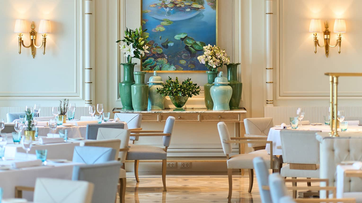 Brightly lit dining room of Riviera with lighted wall sconces, pale blue and white chairs, shiny patterned floor