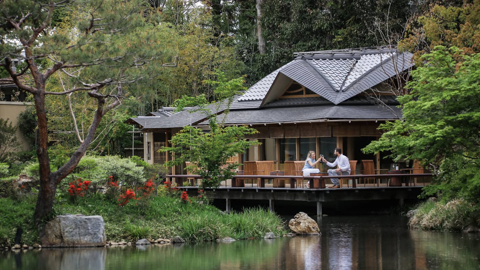 View across pond to restaurant patio where couple toasts with wine glasses