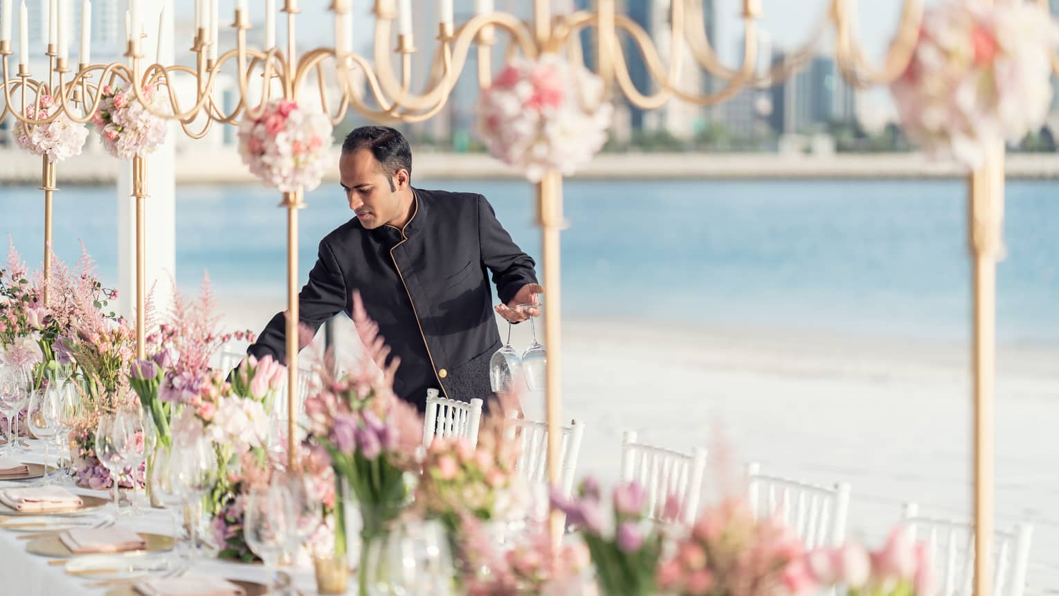 Hotel staff sets long outdoor dining table with row of tall gold candelabras
