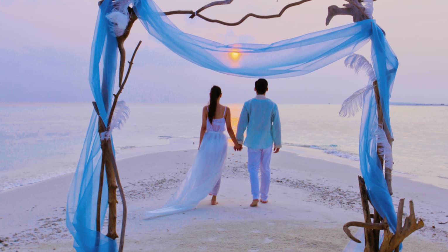 Wedding altar in front of couple walking on Blu Beach at sunset