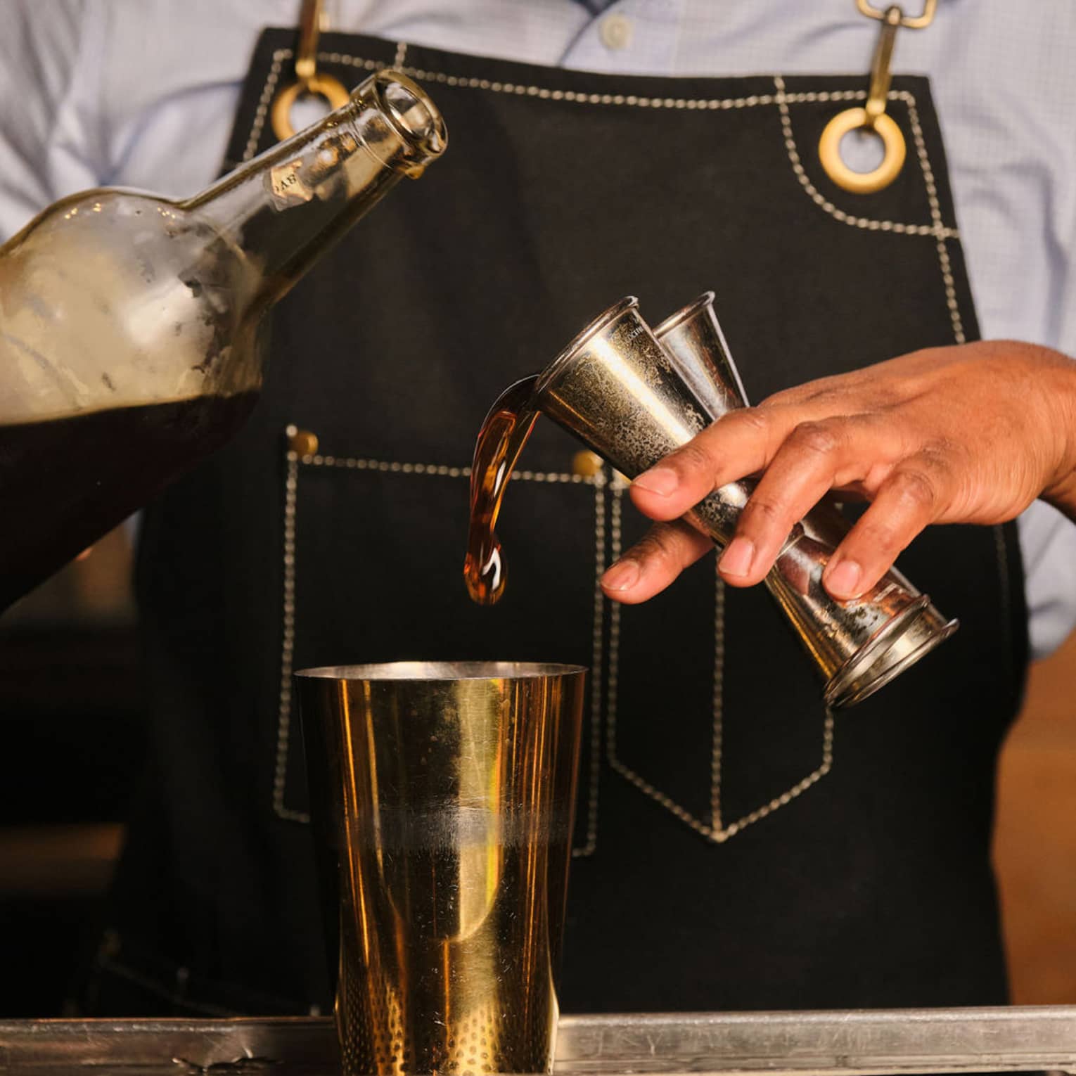A bartender pours liquid from two jiggers into a cocktail shaker