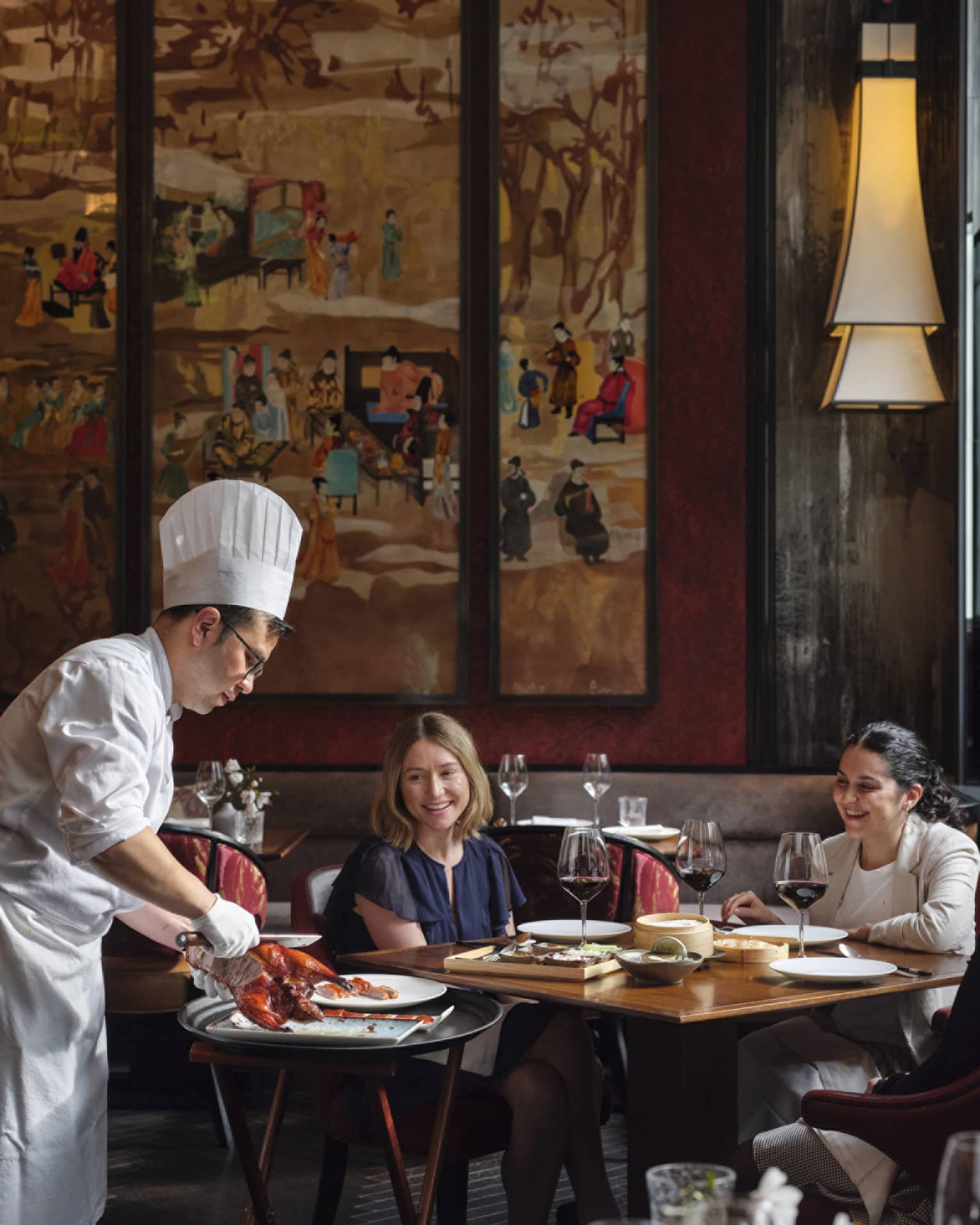 Two women being served food by a chef.