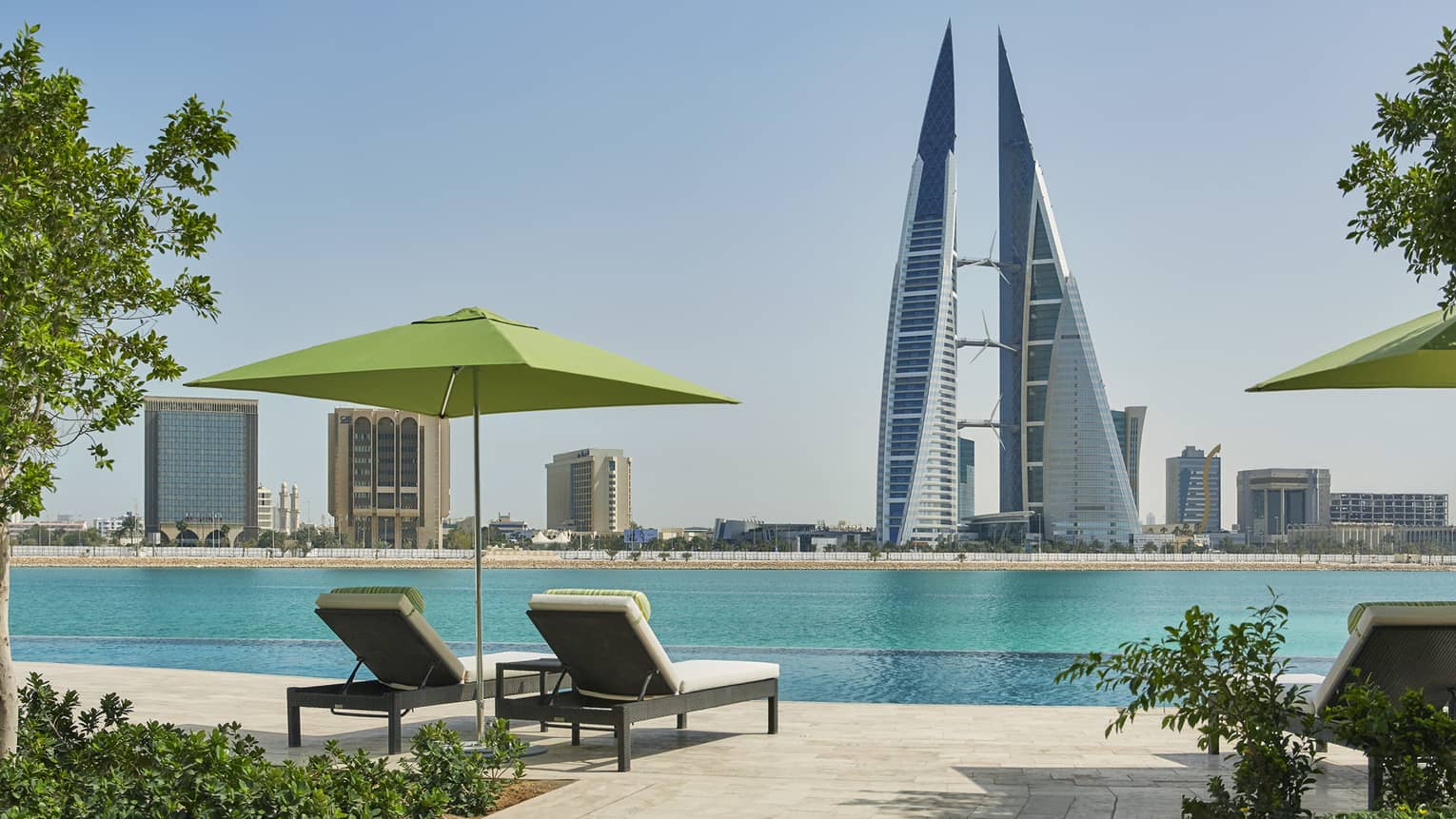 Two lounge chairs under lime-green umbrella on deck looking out at Arabian Gulf, modern tower