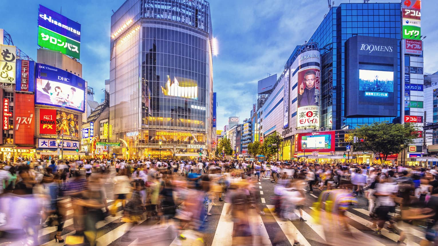 Image of blurry crowds along sidewalk under glass buildings, colourful billboards at night