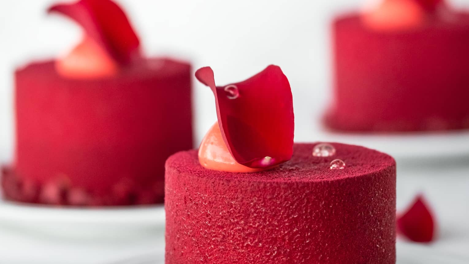 Three bright red mini cakes topped with red flower petals