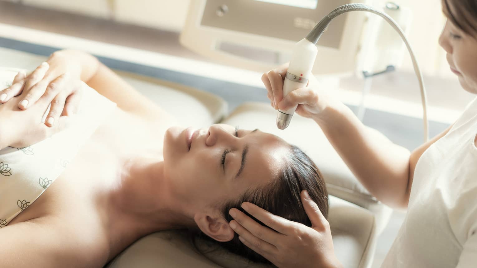 An aesthetician uses a tool on the face of a relaxing woman.