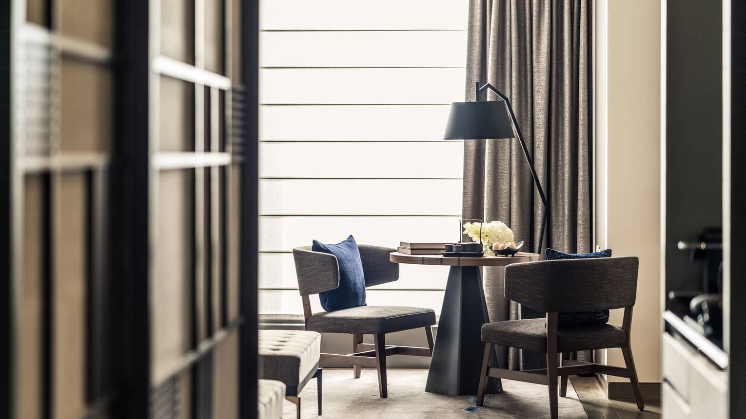 Cozy seating area with two chairs, a round table and a floor lamp, set near a large window
