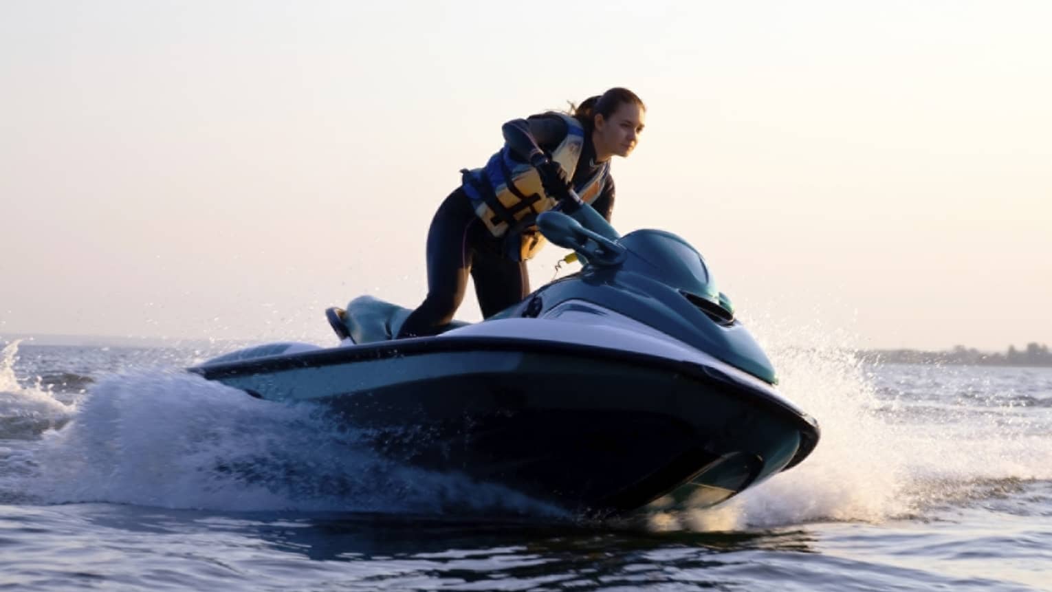 Woman wearing life jacket stands, steers jet ski on ocean at sunset
