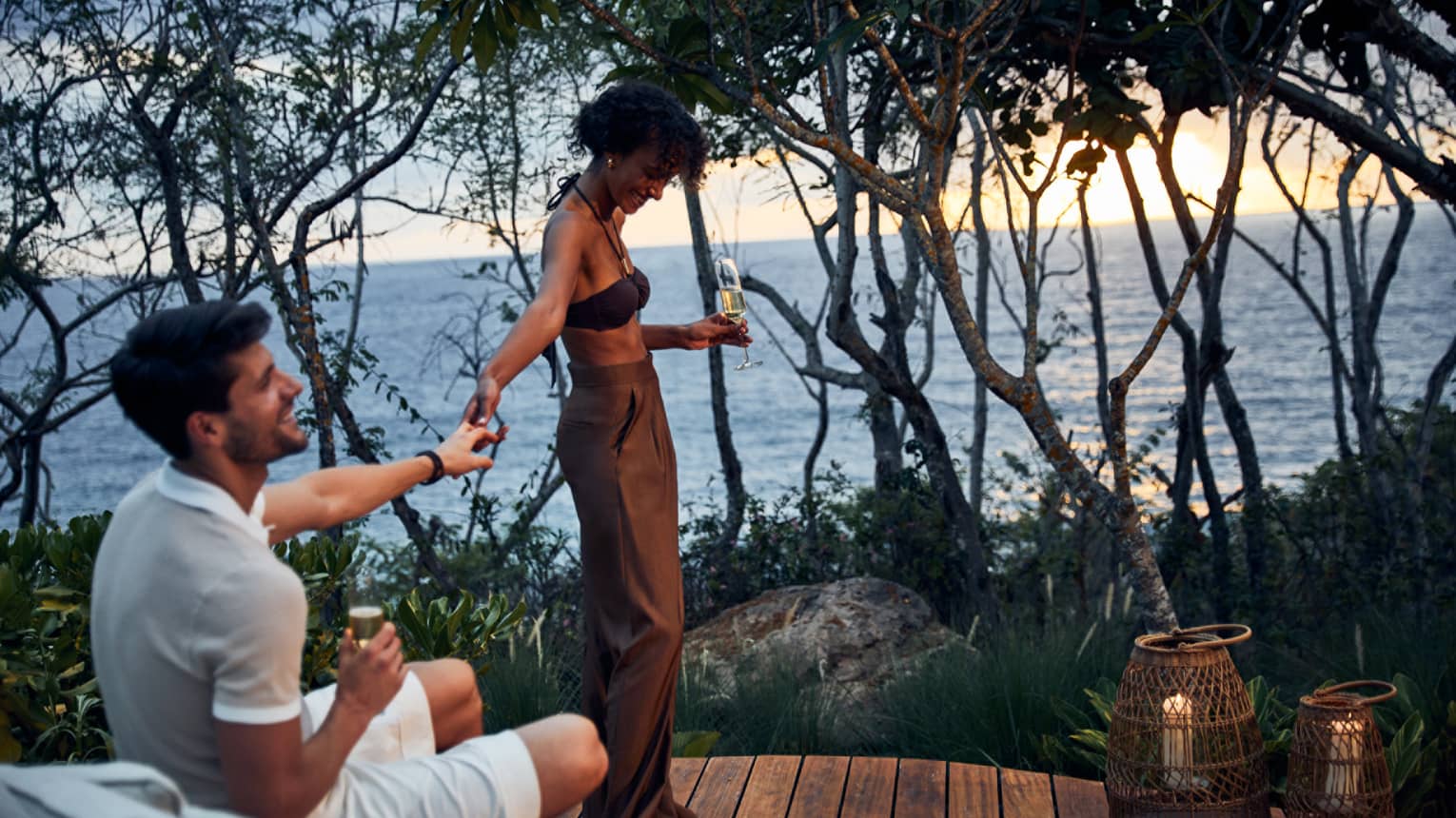 A man and woman resting on a platform outside while drinking wine.