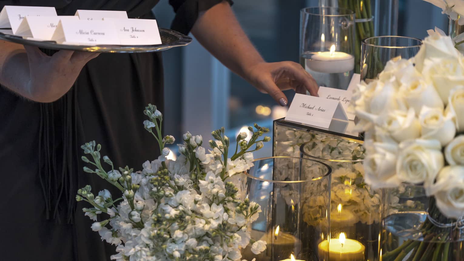Event staff with tray places name cards on elegant banquet table with white flowers, candles