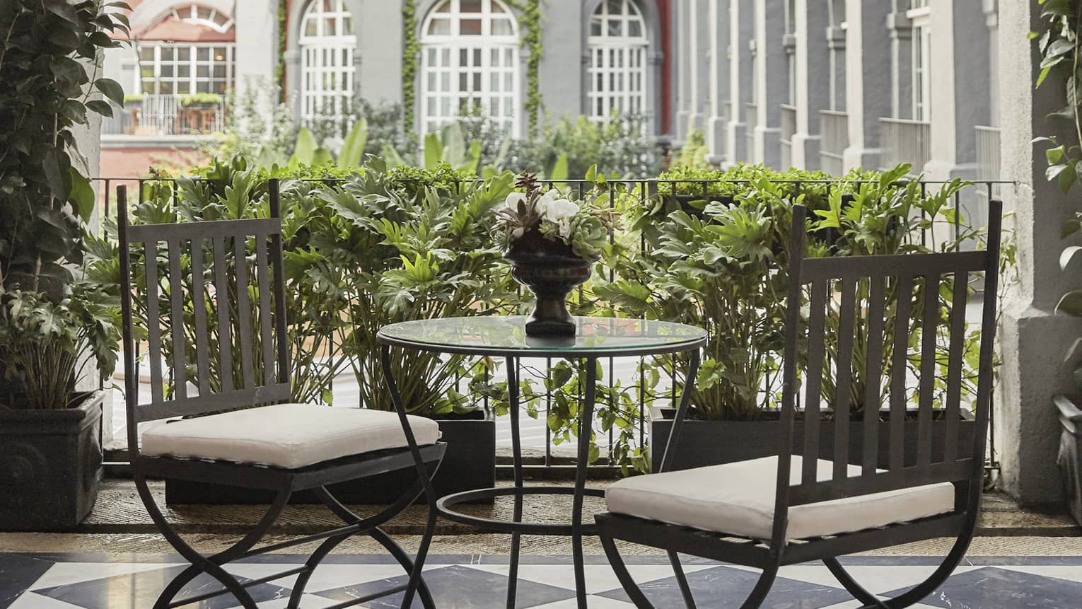 Black-and-white tiled floor of terrace with small table and two chairs, looking out to courtyard