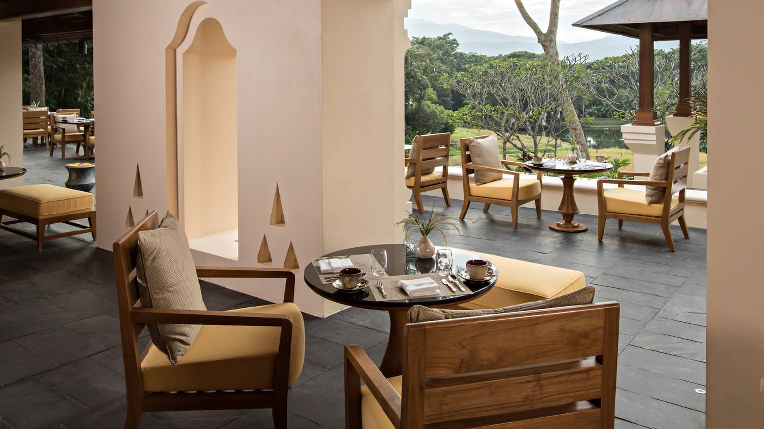 Two wood patio chairs in front of round table, white wall at KHAO restaurant