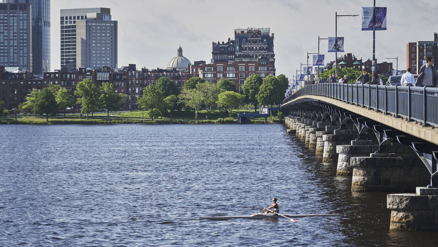A person kayaking on a wide river with a city in the background.