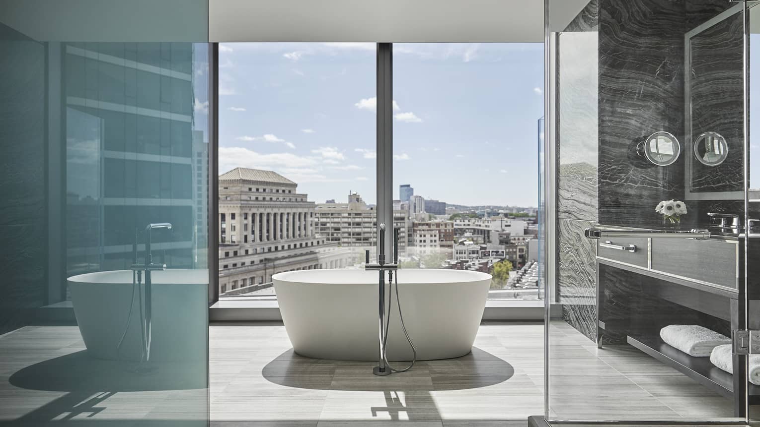 A free-standing tub sits in the middle of a large bathroom, overlooking downtown boston through floor to ceiling windows
