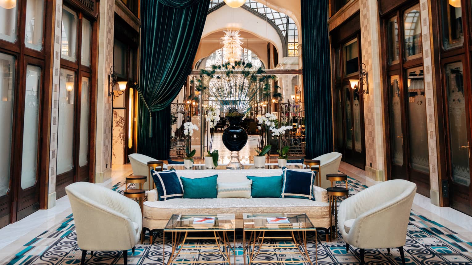 Zrínyi Passage with Zsolnay tiles, white chairs and couch, blue cushions, drapes and high ceiling