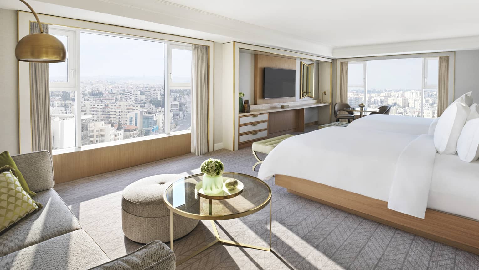 Bedroom with two walls of windows overlooking Amman city. Carpeting and two twin beds.