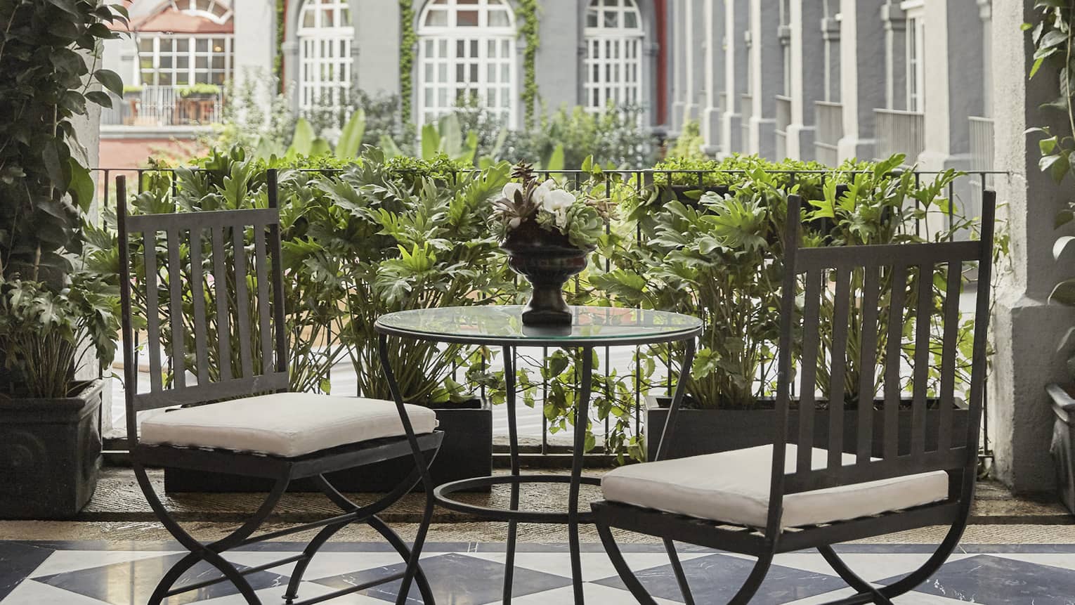 Black-and-white tiled floor of terrace with small table and two chairs, looking out to courtyard