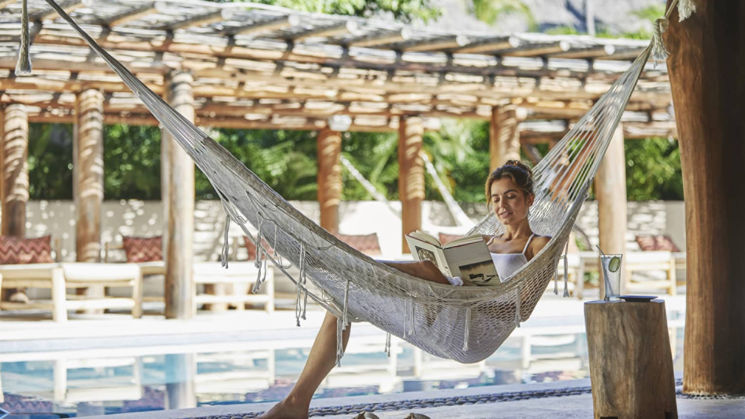 Woman reads book in a hammock next to pool