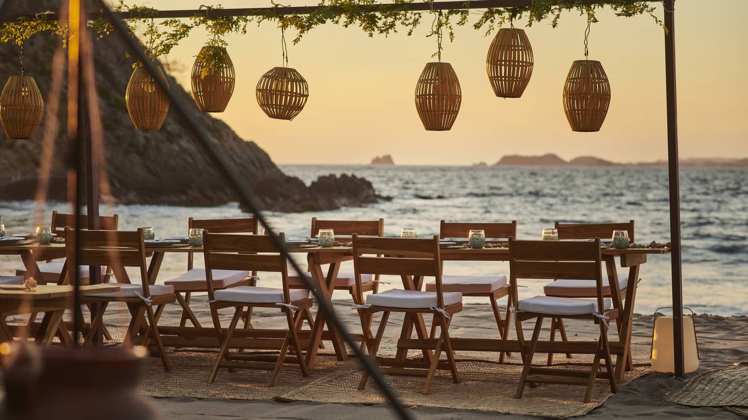 An outdoor private dining table on a beach with lanterns hung above.