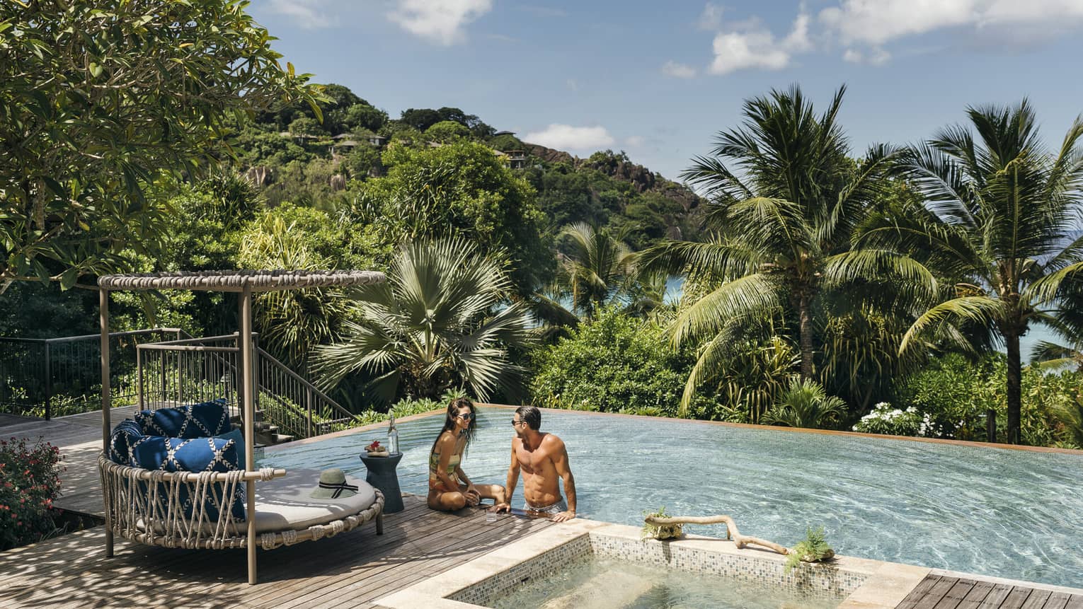 A couple sits by a large infinity pool overlooking the ocean