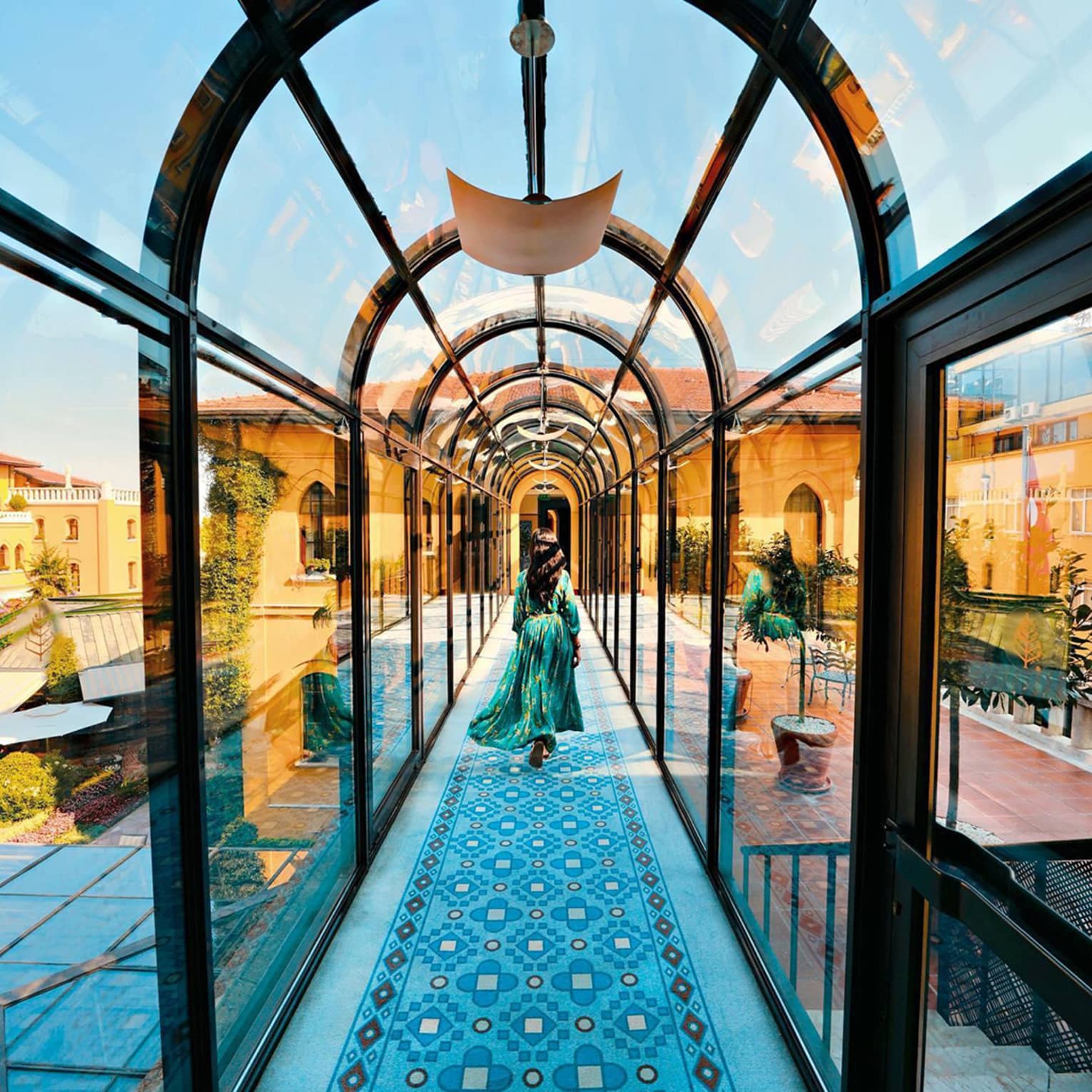Woman wearing flowing dress walks down arched glass hallway