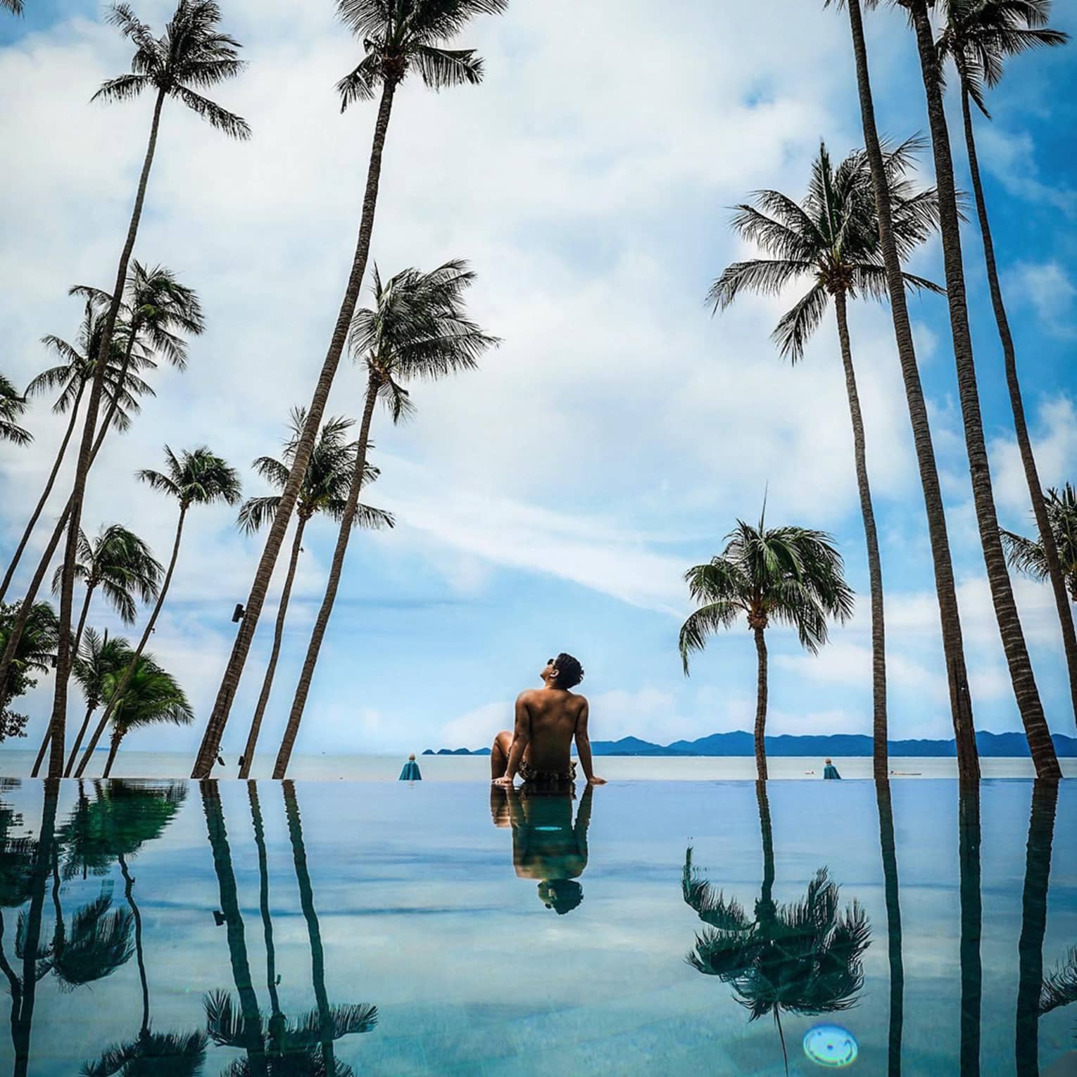 Guest relaxing by the pool surrounded by palm trees