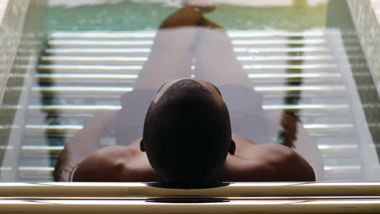 Silhouette of back of man's head, legs in spa tub