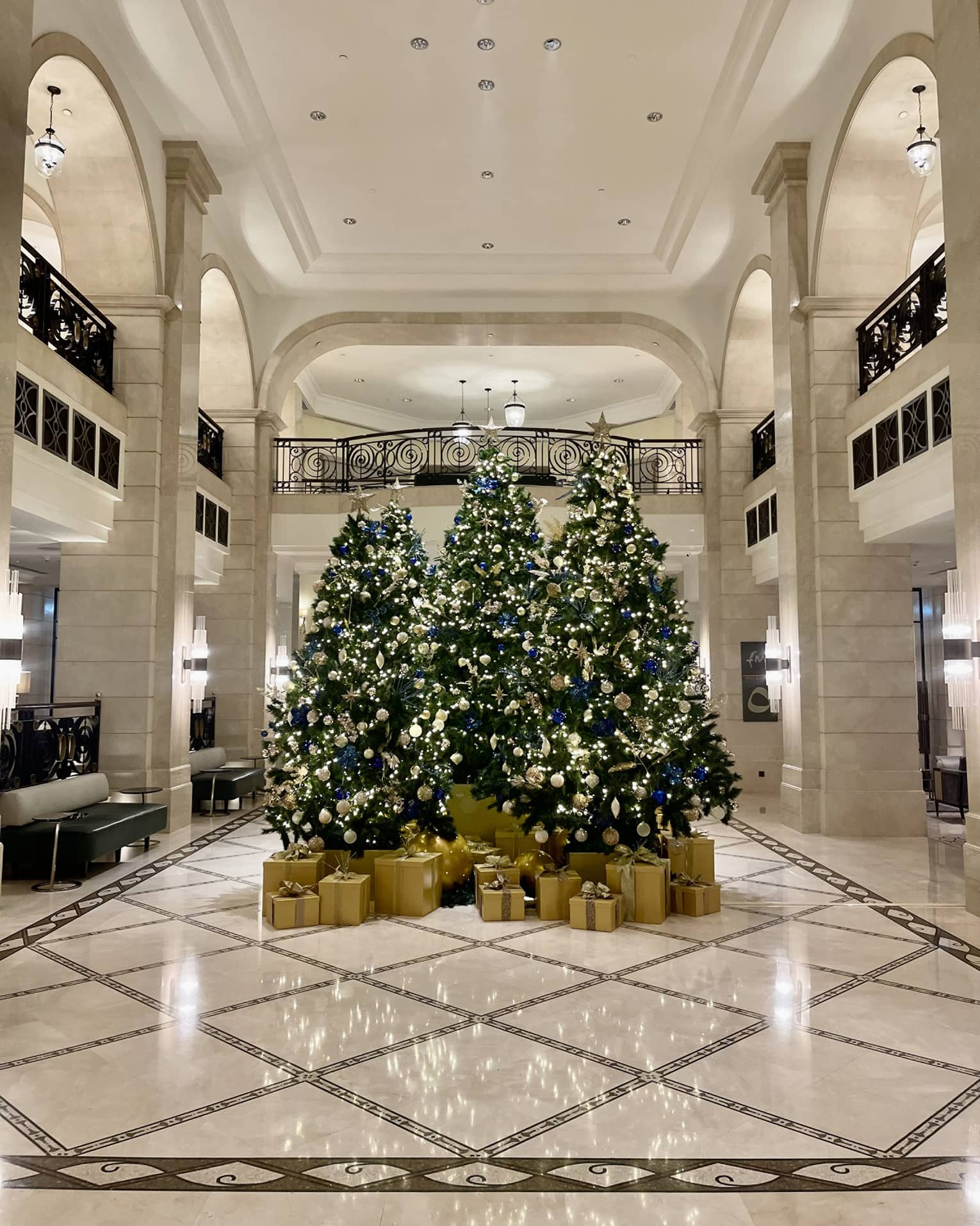 Three Christmas trees decorated in gold sit in the center of the Hotel lobby, with gold-wrapped boxes of presents beneath each one