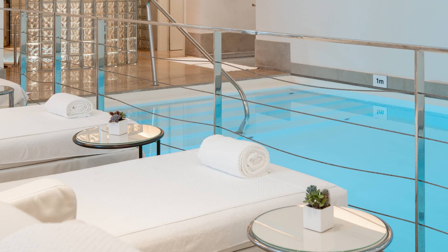 A spacious, well-lit indoor pool area with comfortable poolside spa treatment tables