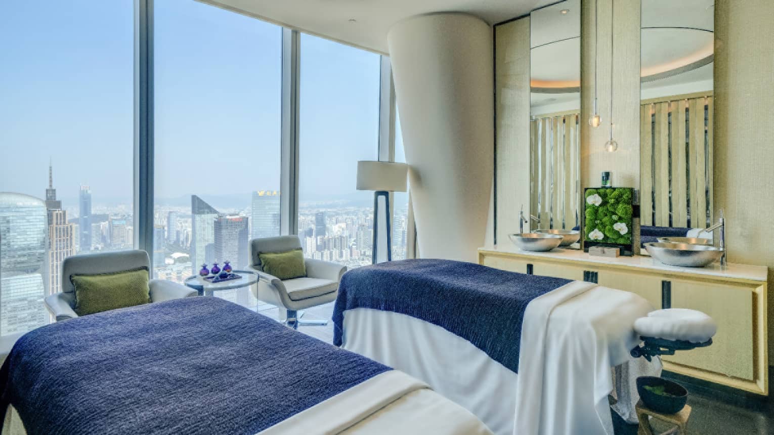 Spa room with twin massage tables, accent chairs, floor-to-ceiling windows with city views